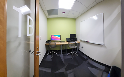 photo of Studio 1A showing a wall-mounted whiteboard and 2 chairs at a desk with an iMac, scanners, and VHS to DVD conversion equipment