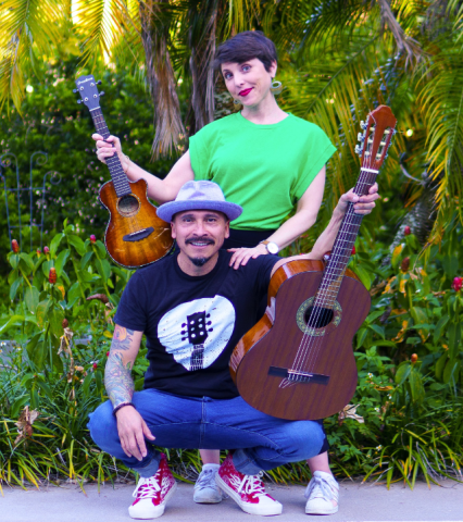 Alina Celeste standing behind Mi Amigo Hamlet while he kneels. She is holding a ukulele and he is holding a guitar.