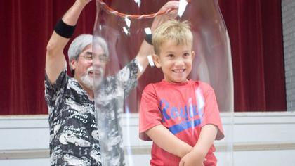 A man putting a young boy inside a liquid bubble. 