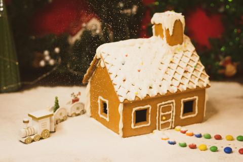 A small house  made of gingerbread with M&M candies leading to the door and powder sugar being dusted on top like snow.