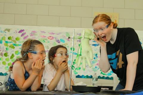 A member of the Talewise team performing a science experiment with two little girl volunteers laughing