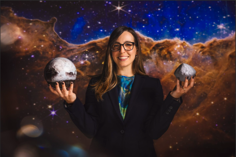 Coralie Adams holding up models of planets with a space background behind her.